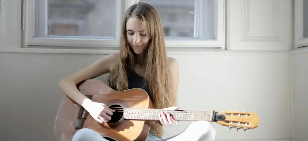 Woman sitting on the floor at home practising acoustic guitar 