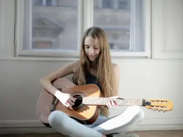 Woman sitting on the floor at home practising acoustic guitar 