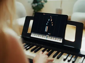 Woman learning to play piano with a piano learning app on a tablet.