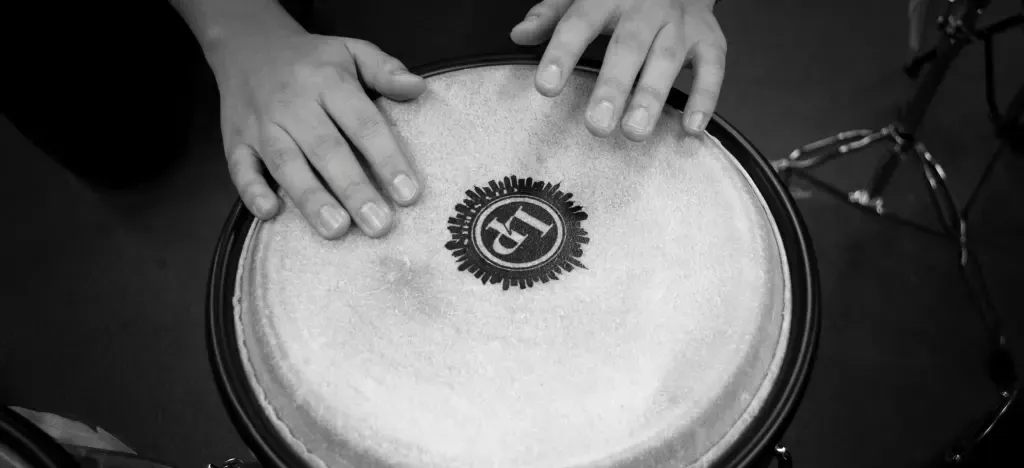 Person playing a drum, developing core musical skills like feeling rhythm, coordinating hands, and listening actively to sound.
