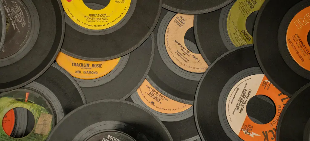 Stack of vintage 45 RPM vinyl records by artists like Neil Diamond, Don McLean, and The Bee Gees — representing classic songs that use popular chord progressions like I–IV–V and I–V–vi–IV.”