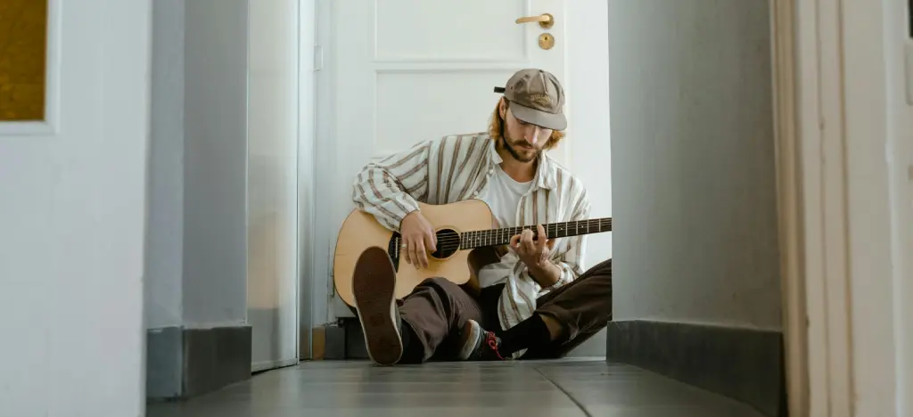 Man relaxing playing acoustic guitar sitting cross-legged. Neurodivergent people often need a different route in — something more visual, more physical, more flexible, or just less rigid.